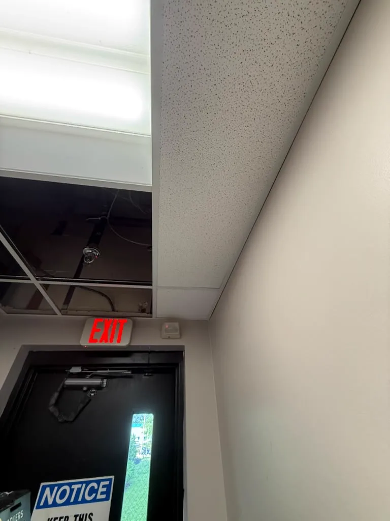 Close detail of new acoustic ceiling tile set against exposed structure above an exit door